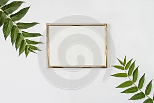 Stylish modern composition. Golden empty frame and green tropical leaves on a white background. Flat lay. Mock up