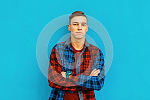 Stylish modern handsome young man in a multi-colored fashionable plaid shirt with hairstyle in a t-shirt posing outdoors