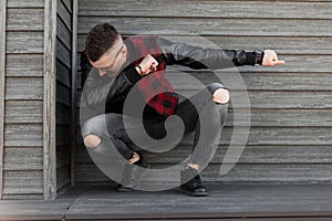 Stylish modern hipster man with a fashionable hairstyle in a trendy red checkered jacket in gray ripped jeans in black sneakers