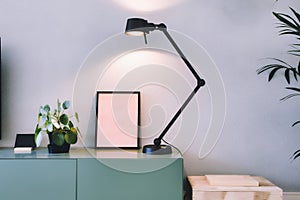 Stylish modern interior, empty picture frame with black lamp and green Chinese Money plant, retro pancake plant on green table