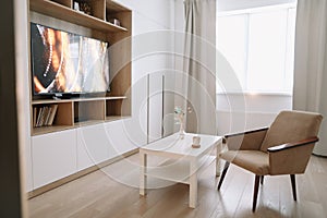 Stylish modern living room interior design with TV, armchair, coffee table and a window with curtains.