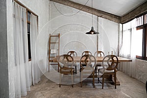 Stylish modern loft dining area with natural light scene and bare concrete wall with natural wood table and chairs setting  /