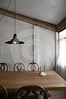 Stylish modern loft dining area with natural light scene and bare concrete wall with natural wood table and chairs setting  /
