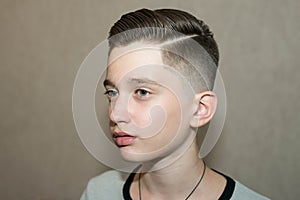 Stylish modern retro haircut side part with mid fade with parting of a school boy guy in a barbershop on a brown background