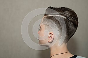 Stylish modern retro haircut side part with mid fade with parting of a school boy guy in a barbershop on a brown background
