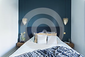 Stylish and modern sunny bedroom interior with small wooden night table , garden in a jar, white bedding, colours pillows.