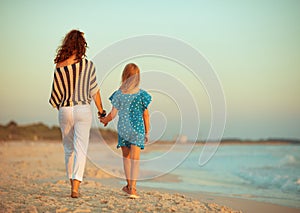 Stylish mother and daughter on seacoast in evening walking