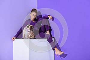 stylish mulatto girl in purple suit sitting on cube with pug dog, ultra violet