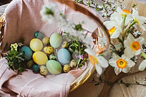 Stylish natural dyed easter eggs with spring flowers on linen napkin in wicker basket. Traditional Easter food. Top view. Rustic