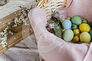 Stylish natural dyed easter eggs with spring flowers on linen napkin in wicker basket. Traditional Easter food. Top view. Rustic