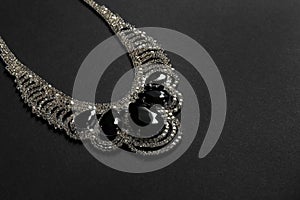 Stylish necklace with gemstones on black background, space for text