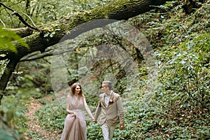 A stylish newlyweds is walking on a trail in a beautiful romantic place on nature. Wedding ceremony outdoors.