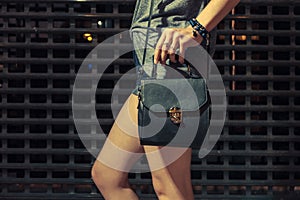 Stylish night fashion portrait of trendy casual young woman with black leather handbag posing near metallic urban wall