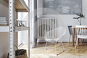 Stylish nordic living room with design armchair, coffee table, white lamp, bookstand, furniture, carpet, plant.