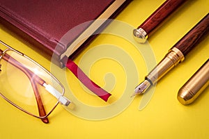 Stylish office still life on yellow table with pen, glasses and notepad