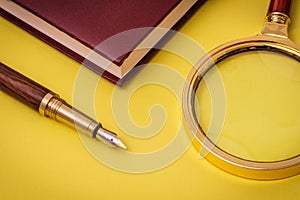Stylish office still life on yellow table with pen, magnifying glass and notepad
