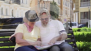 Stylish old couple of travelers sit on bench in foreign city looking at the map