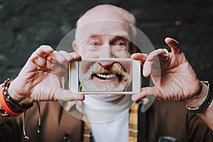 Stylish old man is holding smartphone in hands