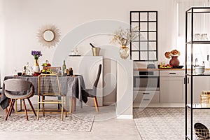 Stylish open plan kitchen and dining room interior with white cupboard and long table with grey tablecloth and food