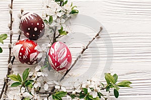 stylish painted easter eggs on rustic wooden background with spring flowers and willow branches. happy easter greeting card flat