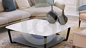 Stylish pastel living room furnished with round marble table, soft grey couch with multiple cushions and comfy armchairs