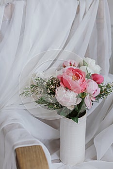 Stylish peonies bouquet on background of soft white fabric, flowers in ceramic vase. Mothers day