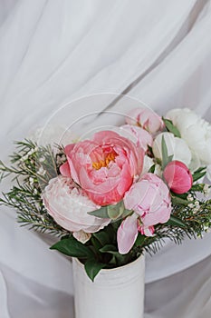 Stylish peonies bouquet on background of soft white fabric, flowers in ceramic vase. Mothers day