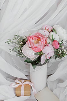 Stylish peonies bouquet, gift, greeting card on background of soft white fabric. Happy Mothers day