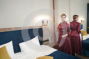 Stylish pin up short hair blonde woman with plus size curvy body posing in fashion red bathrobe near the mirror in the