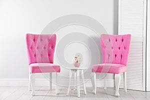 Stylish pink chairs and table near white wall