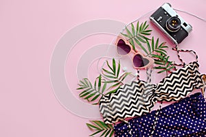 stylish pink sunglasses, modern swimsuit, photo camera,headphones and green palm leaves on pink background, flat lay. space for