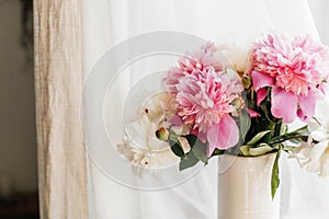 Stylish pink and white peonies in vase. Hello spring. Lovely peony bouquet in sunny light on rustic wooden window sill. Happy