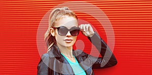 Stylish portrait beautiful blonde woman wearing a black rock jacket and sunglasses on red background