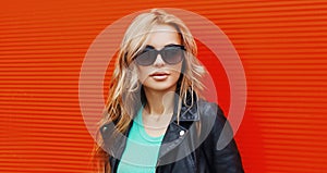 Stylish portrait beautiful blonde woman wearing a black rock jacket and sunglasses on red background