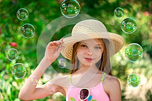 Stylish portrait of smiling girl in hat front of soap bubbles and green background. Summer season