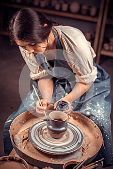 Stylish pottery woman siting on bench with pottery wheel and making clay pot. National craft.