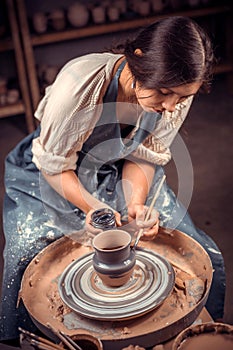 Stylish pottery woman siting on bench with pottery wheel and making clay pot. National craft.