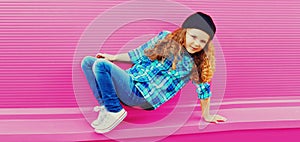 Stylish preteen curly girl dancing in baseball cap on pink background