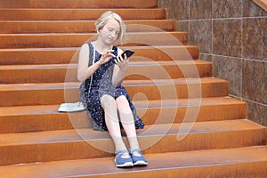 Stylish preteen girl using a phone sitting on a rusty staircase. Child and gadget concept.