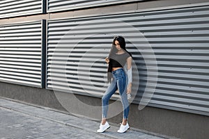 Stylish pretty beautiful young woman in a stylish jacket in a vintage black top in fashionable blue jeans in summer sneakers