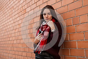 Stylish pretty young woman in a fashion burgundy sweater in fashionable black leather pants with a checked scarf posing in the