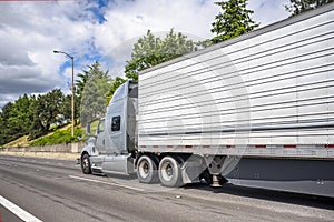 Stylish professional gray big rig semi truck transporting frozen cargo in refrigerator semi trailer running on the straight road