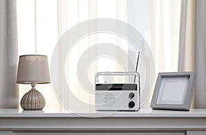 Stylish radio receiver, lamp and frame on white table near window indoors