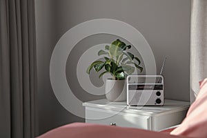 Stylish radio receiver and plant on nightstand in bedroom