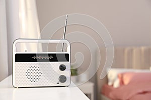 Stylish radio receiver on white table in bedroom, space for text