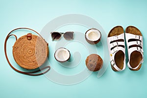 Stylish rattan bag, coconut, birkenstocks, palm branches, sunglasses on blue background. Banner. Top view with copy