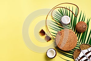 Stylish rattan bag, coconut, birkenstocks, palm branches, sunglasses on yellow background. Banner. Top view with copy