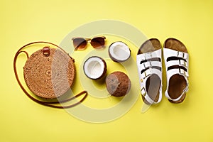 Stylish rattan bag, coconut, birkenstocks, palm branches, sunglasses on yellow background. Banner. Top view with copy