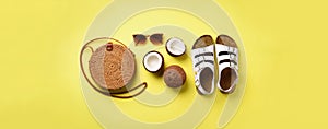 Stylish rattan bag, coconut, birkenstocks, palm branches, sunglasses on yellow background. Banner. Top view with copy