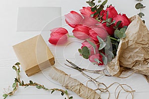 Stylish red tulips bouquet with greeting card, gift, scissors and twine on rustic white wood